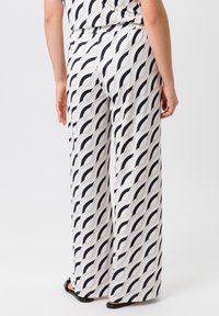 Pantalons larges en tissu léger, avec un motif ondulé noir et blanc. Taille élastique pour un ajustement décontracté, sans fermetures visibles.