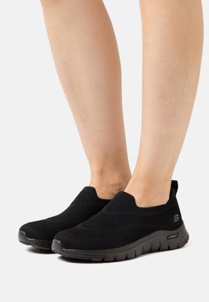 Schwarze Slip-On-Schuhe aus strukturierter Strickware mit niedrigem Schnitt und gepolsterter Sohle, mit einem gebrandeten Logo an der Seite.