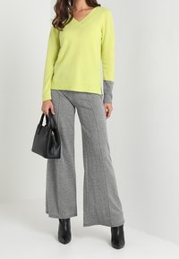 Neon gul v-ringad tröja med grå ärmar, i kombination med vida texturerade grå byxor. En svart handväska och svarta stövlar med klack fulländar outfiten.