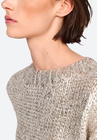 Silberner, strukturierten Strickpullover mit Rundhalsausschnitt und Rippdetail. Das Licht, das von dem Stoff reflektiert wird, verstärkt seine visuelle Anziehungskraft.