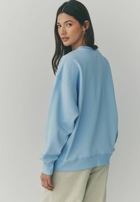 Hellblaues Sweatshirt mit gerippten Bündchen und Saum, mit lockerer Passform. Kombination mit grün-weiß karierten Hosen.