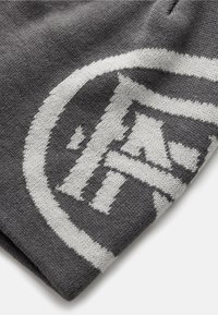 Grijze gebreide stof met een opvallend rond logo in het wit, met een textuurpatroon en contrasterende elementen.