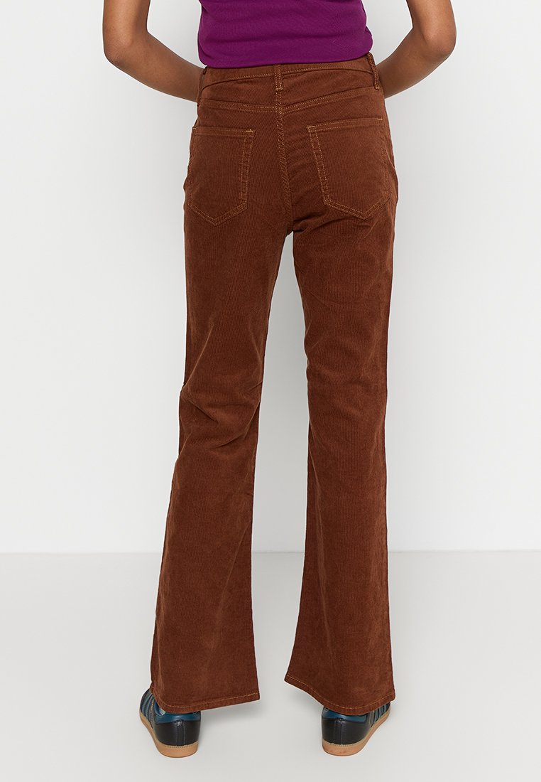 Braune Corduroy-Hose mit Schlag haben eine hohe Taille, zwei Gesäßtaschen und Kontraststickerei. Der Stoff hat ein strukturiertes, geripptes Aussehen.