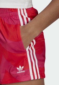 Red athletic shorts featuring a glossy material with a wave pattern, white three-stripe accents, and a small white Adidas logo.