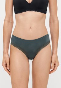 Dark green women's brief with a smooth finish, featuring a scalloped lace trim along the edges. The design is high-waisted and simple.