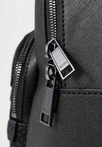 Black backpack featuring textured fabric, dual silver zippers with BOSS branding, and a sleek design. Close-up view highlights hardware details.