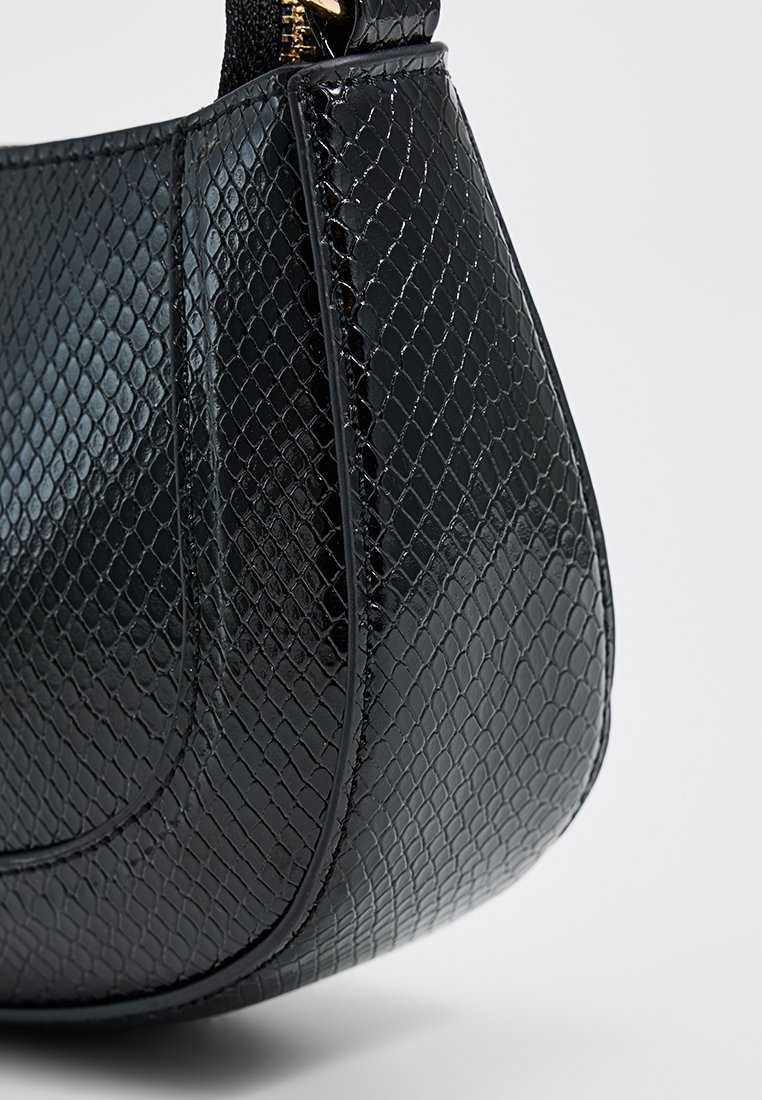 Sac à main noir avec une texture brillante en cuir de serpente, couture visible et tirette dorée sur fond uni.