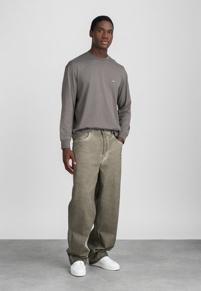 Pelēka garām piedurknēm krekls ar mazu logotipu, kombinēts ar gaiši zaļām platām džinsām un baltām kedām. Vienkāršs dizains, brīvs piegriezums, teksturēta auduma.