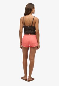Top corto de ganchillo marrón con tirantes finos, combinado con pantalones cortos de mezclilla rosa de cintura alta con dobladillo deshilachado y dos bolsillos traseros.