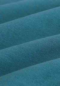 Teal textil med en texturerad, vävd yta. Tyget har diagonala linjer och en mjuk, lätt glansig finish.
