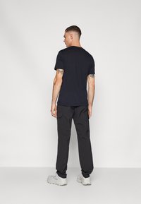 Svart kortärmad T-shirt med rund halsringning, ihop med svarta cargobyxor med sidofickor och ljusgråa sportskor.