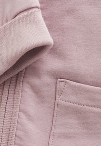 Tissu de sweat-shirt rose clair avec un poignet côtelé et un petit détail de poche brodé. Texture lisse avec un motif tricoté subtil.