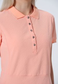 Světlé broskvové polo tričko s texturovaným designem, zapínáním na knoflíky s dekoračními knoflíky a klasickým límcem.