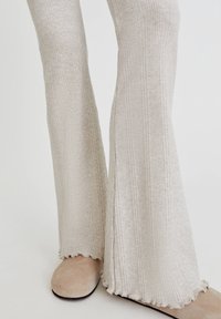 Pantalon évasé beige côtelé avec surface texturée, doté d'un ourlet festonné et assorti à une chaussure douce beige, semblable au daim.