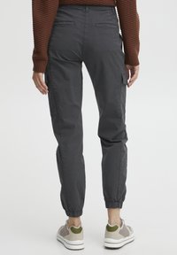 Mørkegrå cargo bukser med sidelommer, elastiske mansjetter og en glatt tekstur, kombinert med lyse sneakers med grønne detaljer.