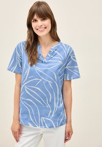 Top azzurro chiaro a maniche corte con scollatura a V, caratterizzato da motivi bianchi a foglia. Il tessuto appare liscio e morbido, con una vestibilità rilassata.