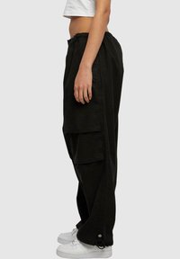 Pantalons cargo noirs avec une taille élastique, poches latérales et une coupe décontractée. Présente un accent à cordon au niveau du poignet et un tissu texturé.