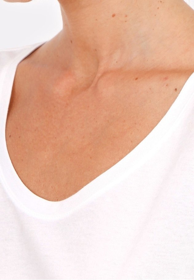 Gros plan sur le décolleté nu et la partie supérieure de la poitrine d'une personne portant un t-shirt blanc à col en V sur fond blanc.
