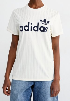 Kremstribet Adidas t-shirt med korte ærmer og rund halsudskæring, med en fremtrædende sort logo på forsiden.