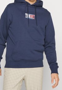 Navy blue hoodie made of cotton blend, featuring a front pocket, drawstring hood, and a logo in red and white on the chest.
