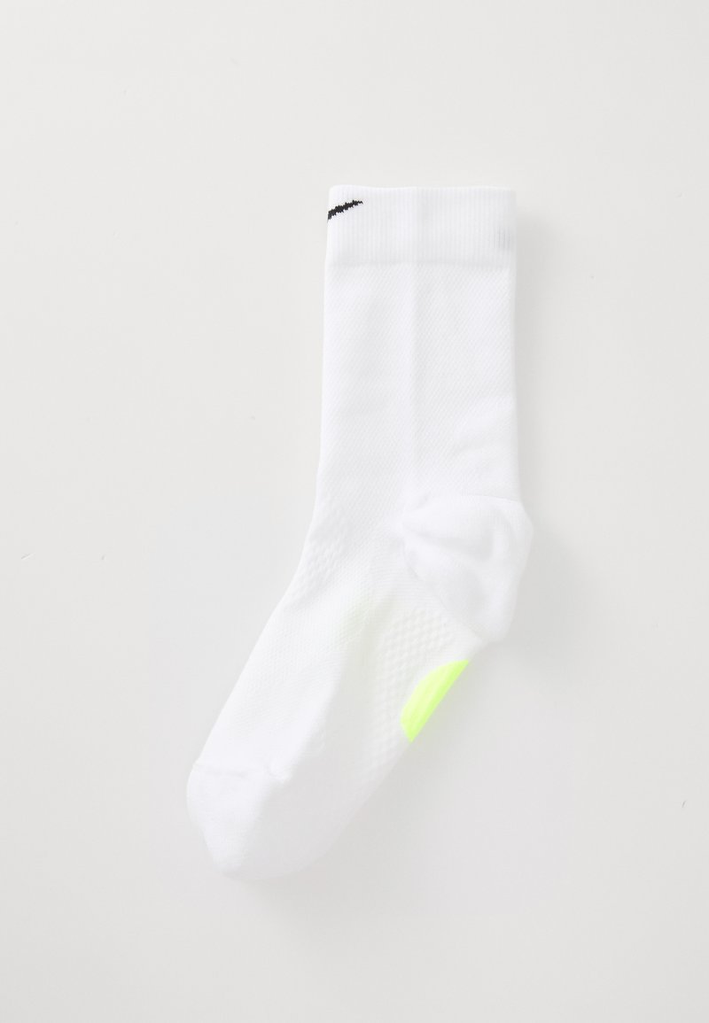 White mid-calf Nike sock with black swoosh near cuff and small neon yellow patch on sole, displayed flat on white background.