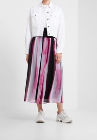 Vit kort denimjacka över en svart topp, ihop med en lång, flödande kjol med vertikala ränder i rosa, lila och svart.