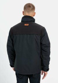 Sort isoleret jakke med høj krave, kontrasterende skulderpaneler og en lædermærke på ryggen.