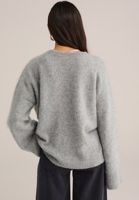 Jasnoszary, miękki sweter wełniany o luźnym kroju, z prążkowanym dołem i opadającymi ramionami. Tkanina ma puszystą teksturę.