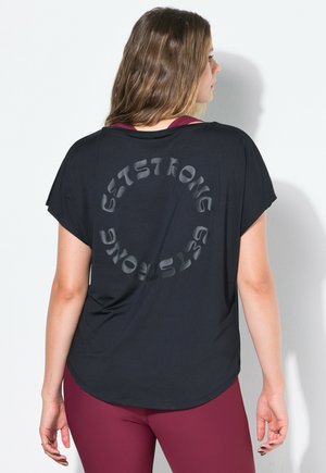 Kvinde vendt væk iført en sort løs t-shirt med teksten "EST STRONG" i cirkulært design på ryggen og maroon farvede leggings.