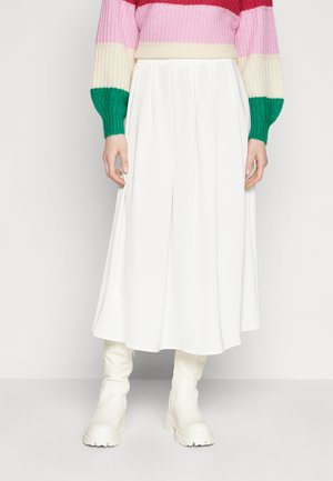 White midi skirt with pleats, paired with a multi-colored knit sweater featuring stripes in pink, red, and green. White chunky ankle boots.