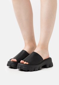 Chanclas negras con un diseño de punta abierta, que cuentan con una suela de plataforma gruesa y texturizada y un empeine de cuero suave para un aspecto moderno.