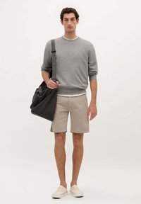 Suéter de punto gris, pantalones cortos beige y zapatillas crema. Bolso de hombro negro con diseño fruncido. Conjunto simple y casual sobre un fondo neutro.