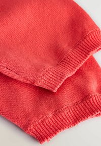 Poignets en tricot corail, avec des bords côtelés et une finition texturée, en tissu lisse sans motifs ni accents visibles.