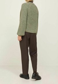 Gebreide groene trui met een losse pasvorm en brede mouwen, gecombineerd met donkerbruine broek en zwarte schoenen. De textuur lijkt chunky.