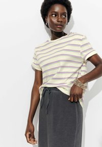 T-shirt à manches courtes rayé de couleur jaune clair avec des rayures lilas et rose foncé, assorti à un pantalon de survêtement gris foncé à cordon.