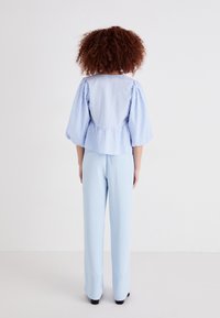 Μπλε καρό μπλούζα με φουσκωτά μανίκια, ζώνη σε στυλ πεπλασμένου, συνδυασμένη με ανοιχτό γαλάζιο παντελόνι σε ίσια γραμμή. Λειαντικός ύφασμα και απλός σχεδιασμός.