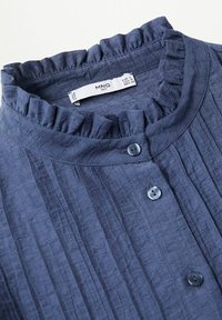 Blouse bleu marine avec col à volants, plis verticaux et boutons foncés, affichant l'étiquette de marque MNG et la taille small.
