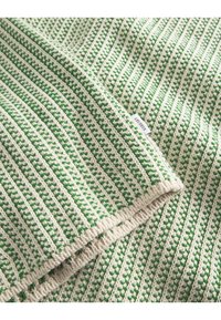Coperta lavorata a maglia con righe verdi e crema e un motivo a rilievo. Presenta un bordo cucito e una piccola etichetta sul lato.