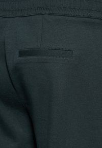 Zbliżenie ciemnych spodni z tkaniny pokazujących tylną kieszeń z patką oraz elastyczny pas ze widocznymi szczegółami szwów.