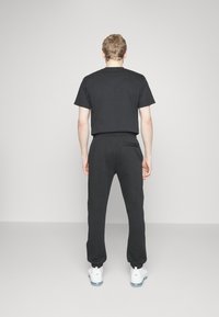 Camiseta negra de manga corta, combinada con pantalones jogger negros que tienen un bolsillo trasero, llevados con zapatillas blancas. Diseño minimalista.