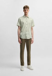 Camicia a maniche corte verde chiaro con motivo floreale, abbinata a pantaloni verde oliva e sneakers bianche. Tessuto morbido, design con bottoni.
