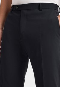 Schwarze, maßgeschneiderte Hose mit glatter Textur, ausgestattet mit einem Knopfverschluss und vorderen Falten, entworfen für eine taillierte Silhouette.