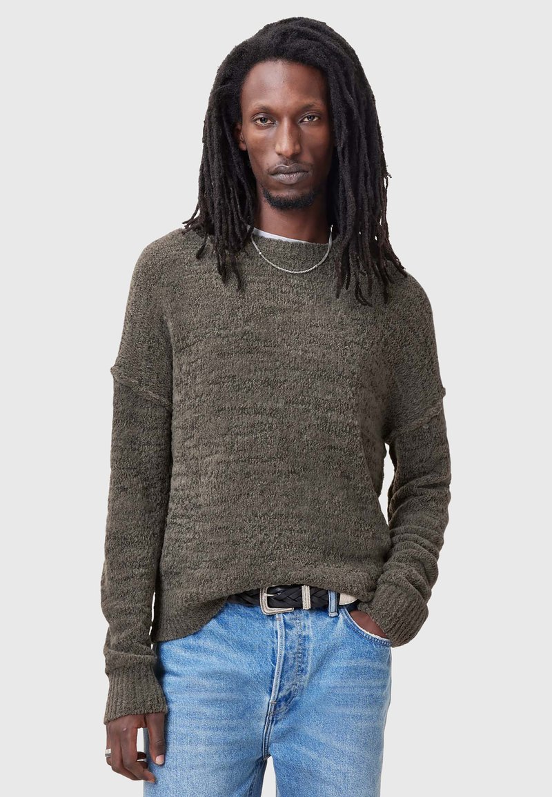 Dark green sweater with a textured knit design, relaxed fit, drop shoulders, and long sleeves, paired with blue jeans and a black belt.