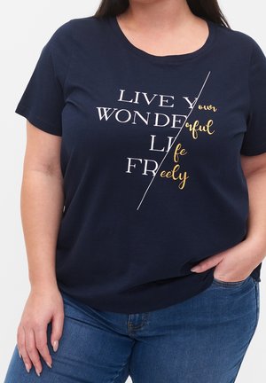 Mørkeblå T-shirt med tekst i blandede skrifttyper: "LEV DIT VIDUNDERLIGE LIV FRIT," båret af en person med den ene hånd i lommen og den anden afslappet.