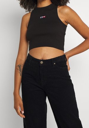 Top court noir avec une texture côtelée et un col haut, arborant un petit logo coloré. Associé à un pantalon en velours côtelé noir taille haute.