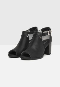 Black peep-toe shoes with a textured perforated finish, ankle strap with a buckle, and a solid block heel.