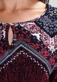 Musteroberteil mit geometrischen Formen in Rot, Weiß und Marineblau. Keyhole-Ausschnitt mit kontrastierenden, detaillierten Designs. Weiche Stoffstruktur.