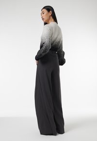 Grijs en zwart ombre trui met lange mouwen, gecombineerd met hoge zwarte wijde broek met een gestructureerde afwerking.