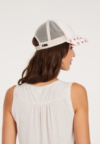 Lkw-Fahrer-Cap mit einem weißen Netzrücken und einem gemusterten rosa Schirm. Verstellbarer Riemen hinten; dezentes Logoetikett an der Seite.