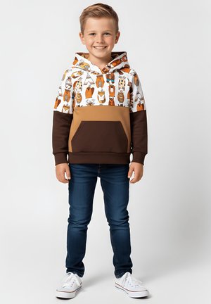 Bluza z kapturem z białym górnym fragmentem z grafikami zwierząt, brązową dolną częścią i przednią kieszenią; w połączeniu z ciemnoniebieskimi dżinsami i białymi butami.